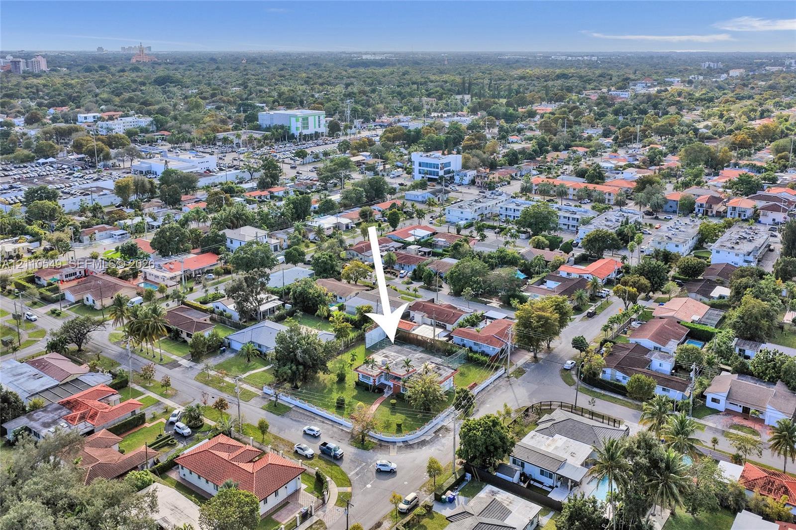 Corner-lot property featuring a multi-pitched roof, paved driveway, mature perimeter landscaping, and a central lawn area