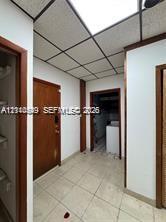 Interior space featuring neutral tile flooring, wood-finish doors with matching door frames, and a drop ceiling with integrated lighting panels
