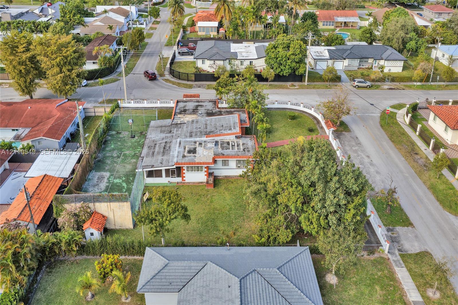 Corner lot property featuring an enclosed multi-use sports court, expansive green space, mature trees, and perimeter fencing