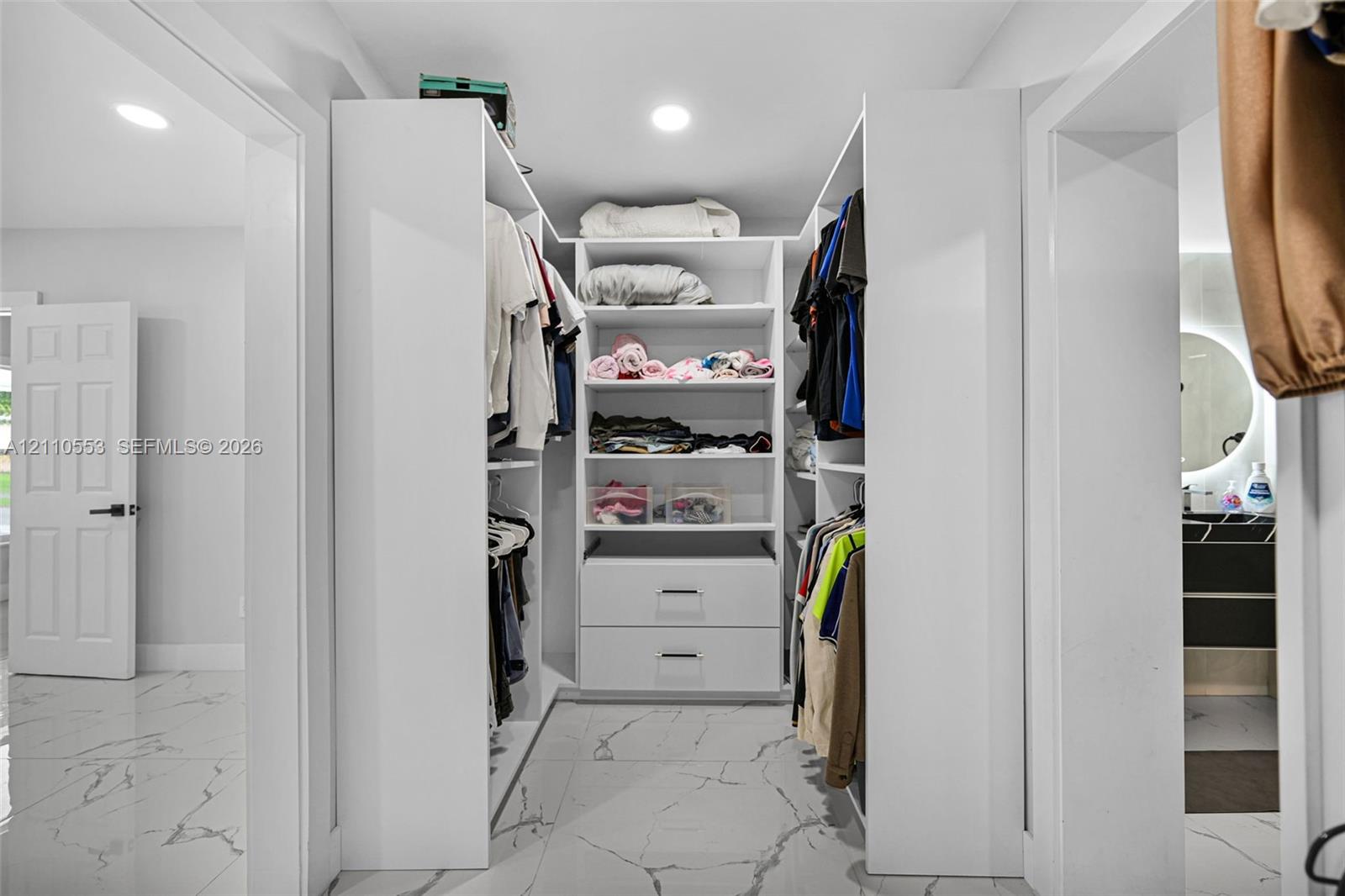 Walk-in closet featuring custom white built-in shelving, integrated dresser drawers, recessed lighting, and large-format tile flooring