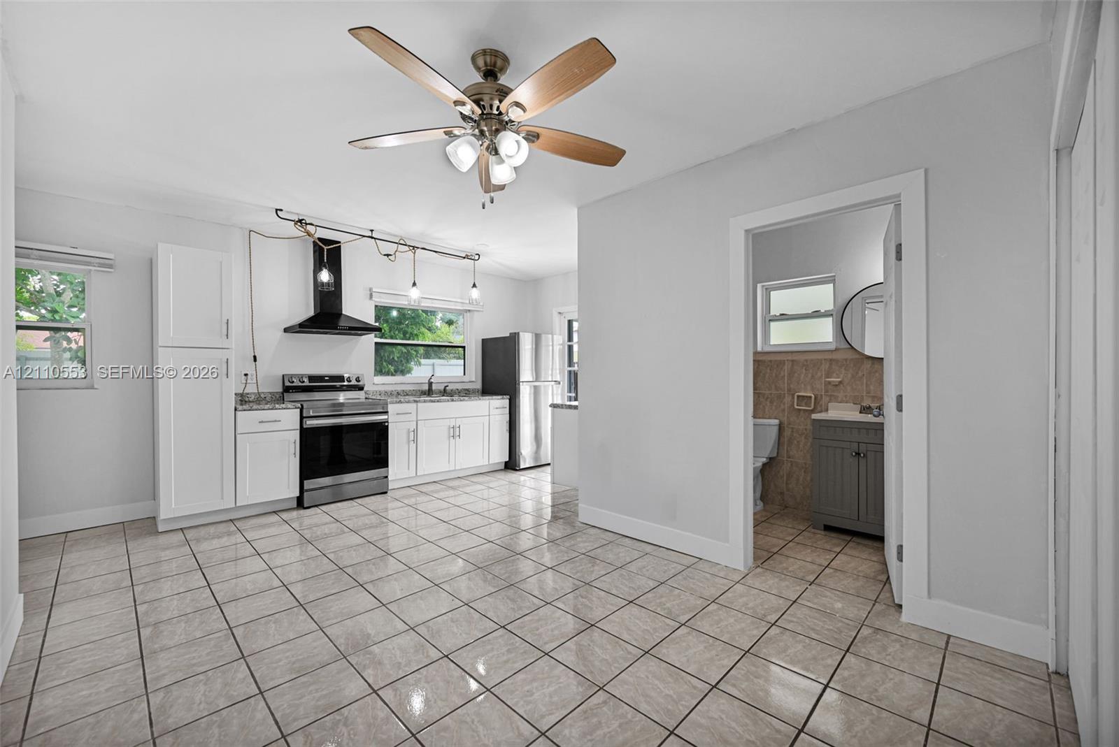 Kitchen featuring white cabinetry, stainless steel appliances, a black range hood, tile flooring, and a ceiling fan with integrated lighting