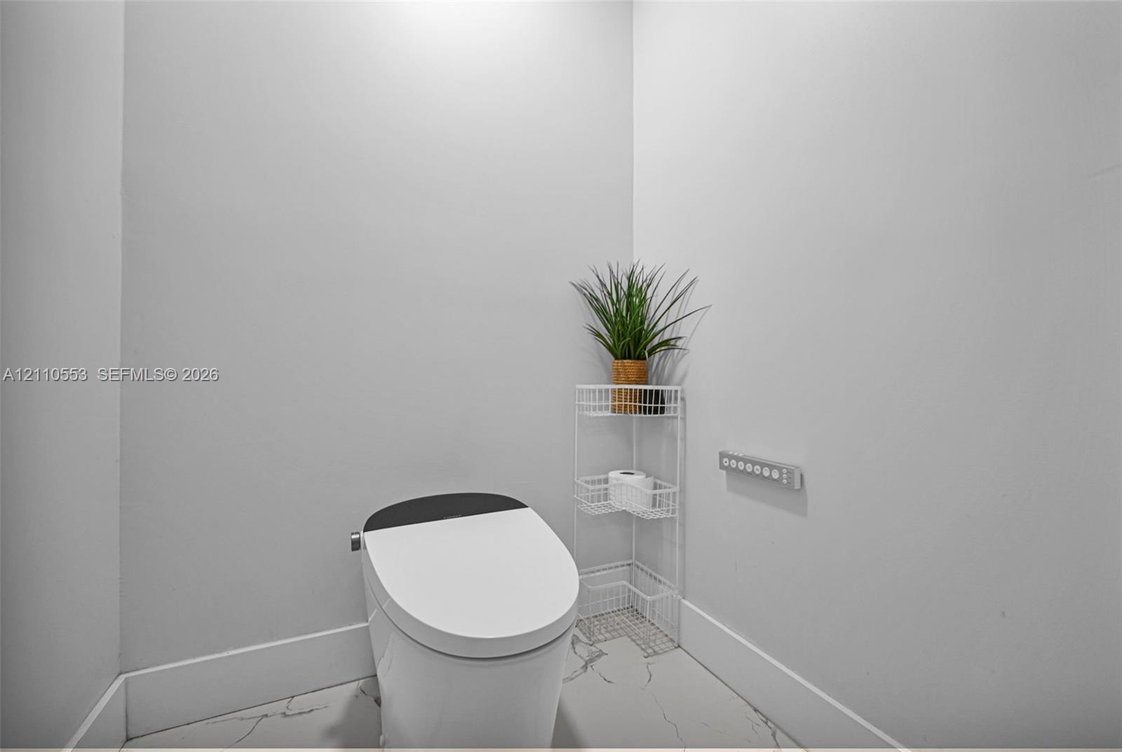 Modern one-piece smart toilet featuring a streamlined profile and contrast lid, set against large-format tile flooring with marble-finish veining and wall-mounted digital control panel