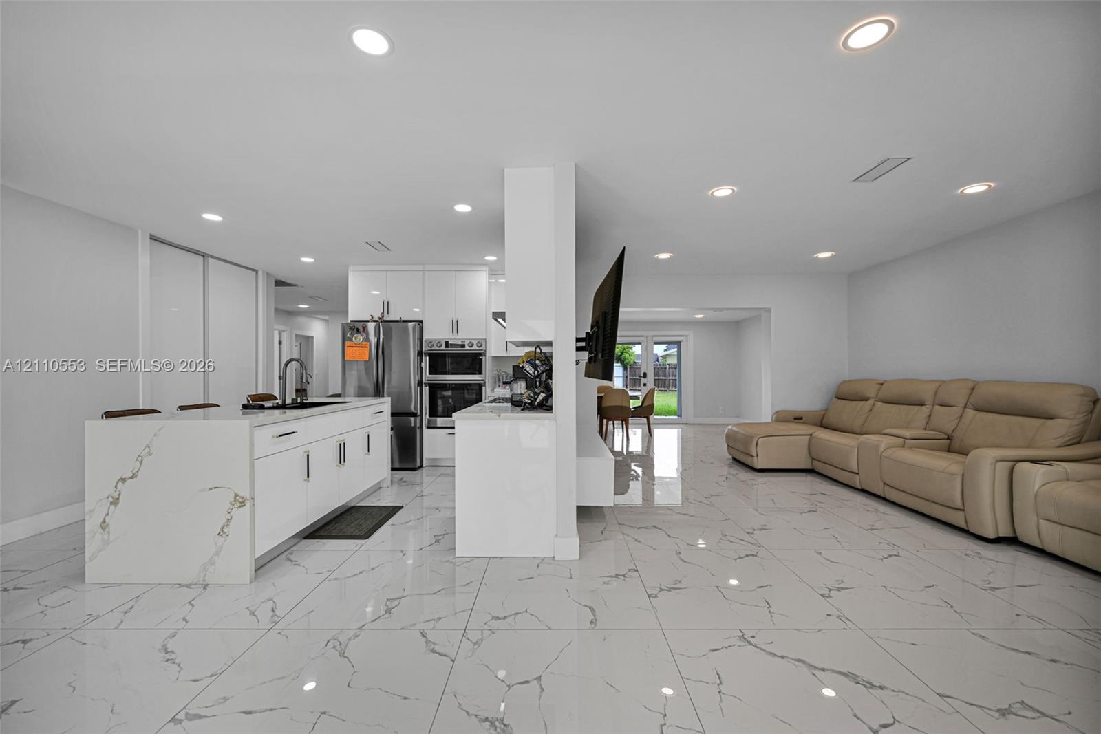Kitchen area featuring an island with a waterfall countertop, white flat-panel cabinetry, recessed lighting, and large-format tile flooring