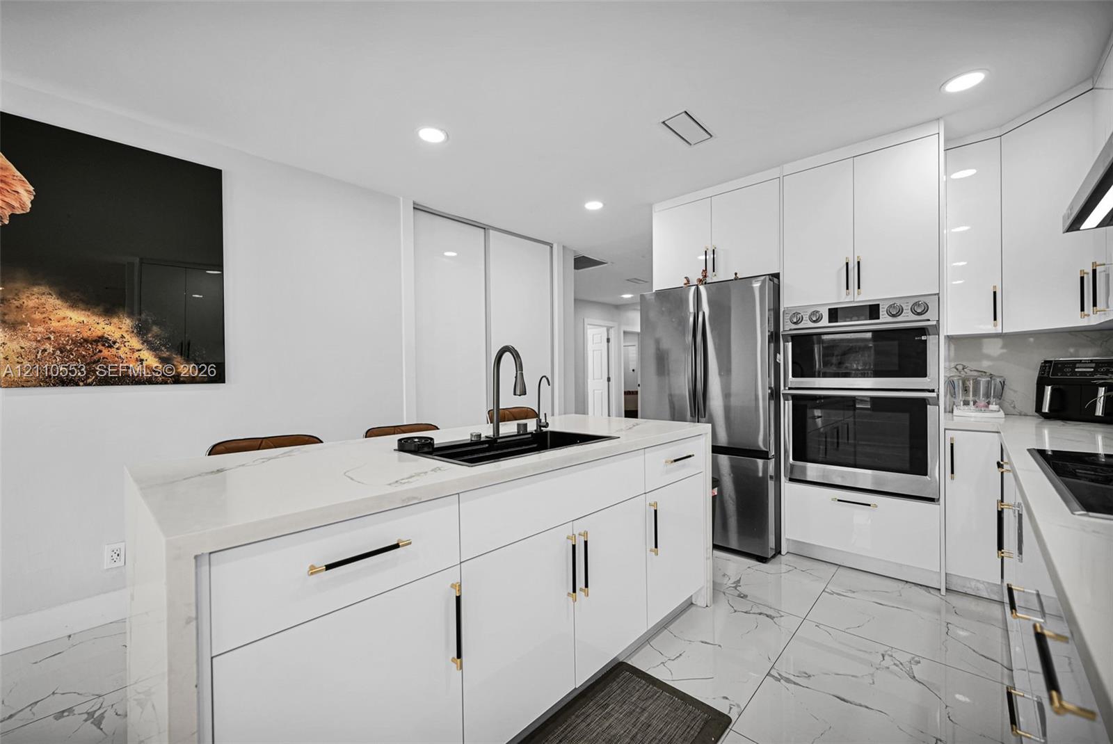 Kitchen featuring high-gloss white cabinetry, white stone-finish waterfall edge island, stainless steel double wall oven, integrated refrigerator, and large-format tile flooring