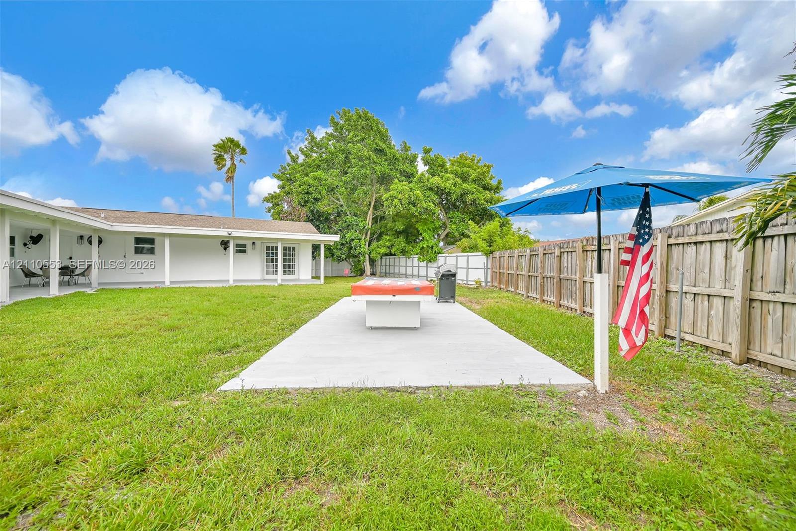 Expansive backyard featuring a concrete patio, a covered porch, and wood-panel fencing