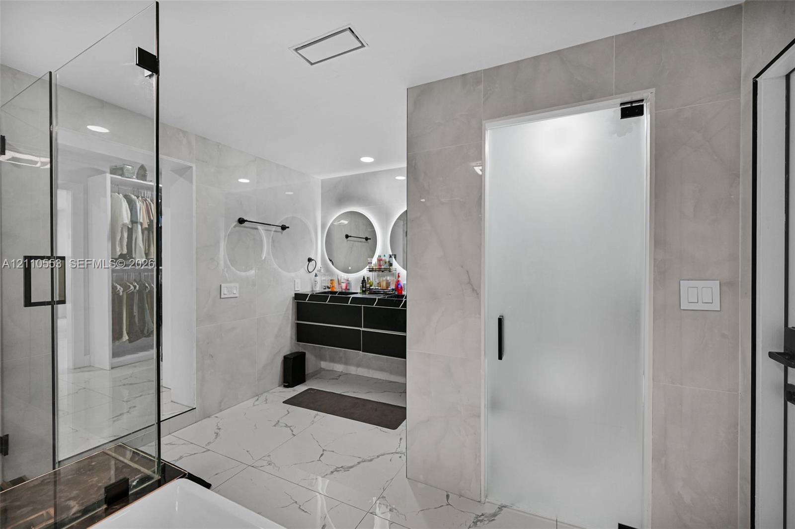 Large-format tiled flooring, wall-to-wall stone-finish wall tiling, dual floating vanity with integrated lighting, glass-enclosed shower, and frosted glass privacy door