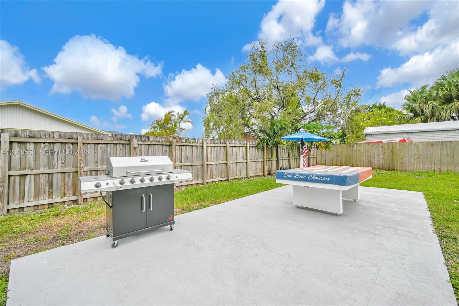 Spacious backyard featuring a large concrete patio, privacy wood fencing, and mature landscaping