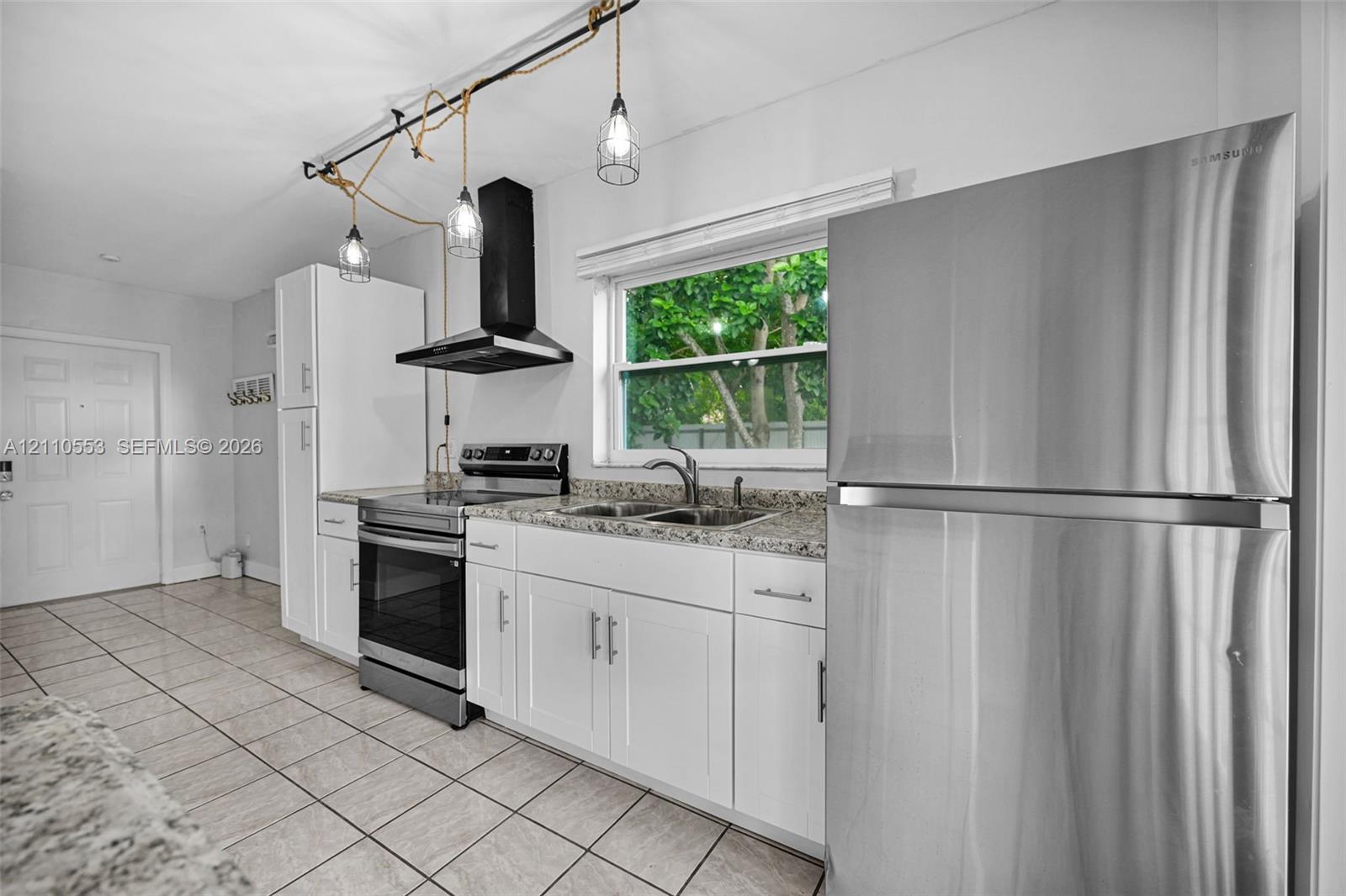 Kitchen featuring white cabinetry, stone-finish countertops, stainless steel appliances, tiled flooring, and industrial-style pendant lighting