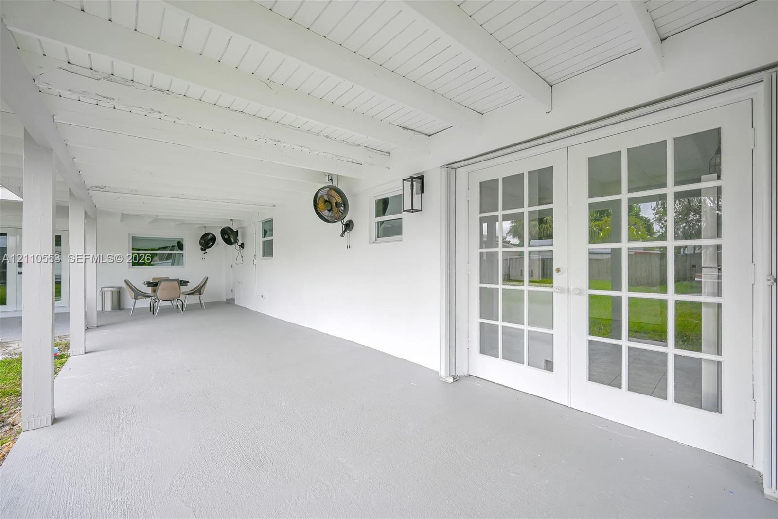 Covered patio featuring a painted wood-beam ceiling, glass-paned French doors, exterior wall-mounted lighting, and concrete flooring