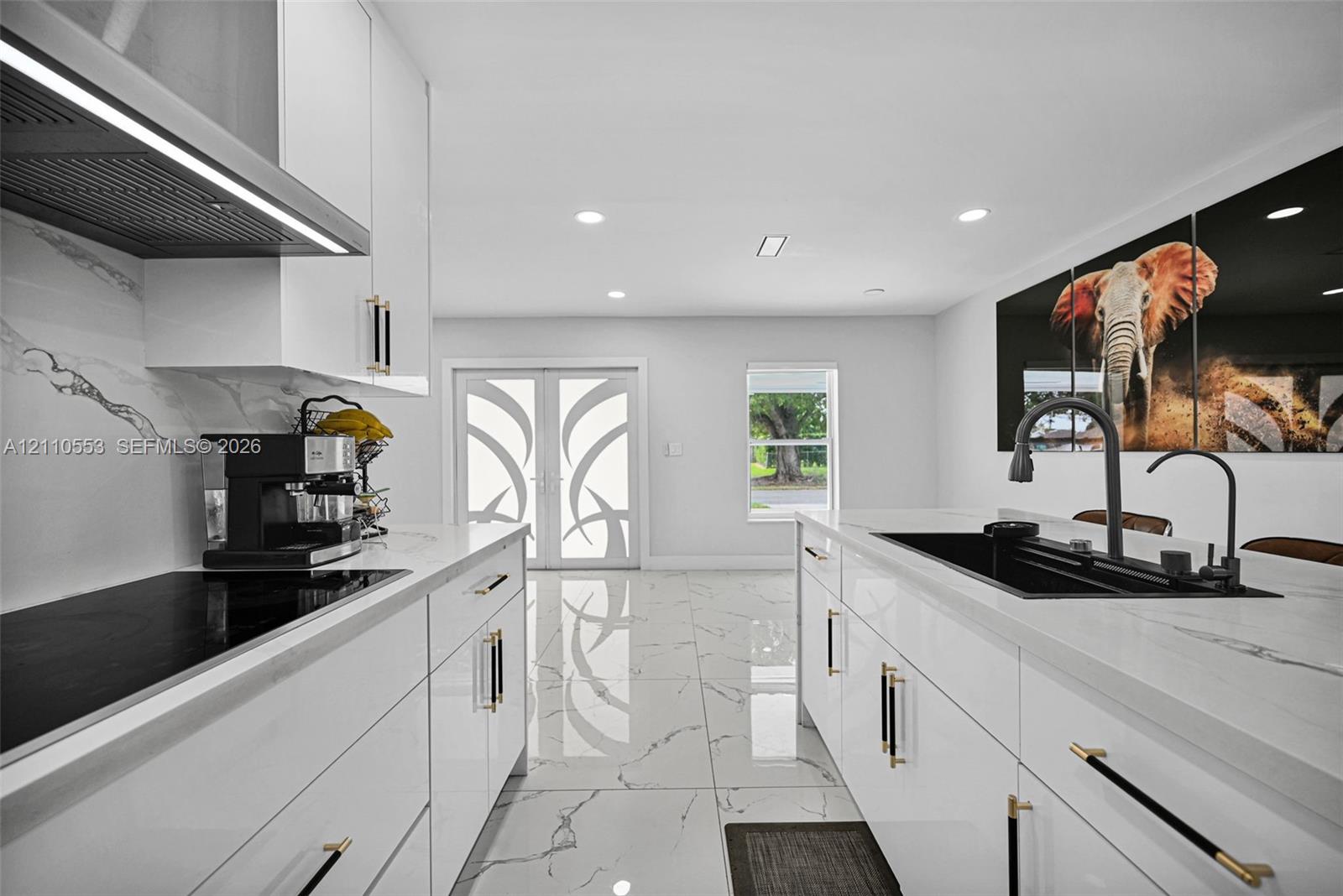 Kitchen featuring high-gloss cabinetry, stone-surface countertops, large-format tile flooring, a center island with an integrated sink, and matte hardware accents