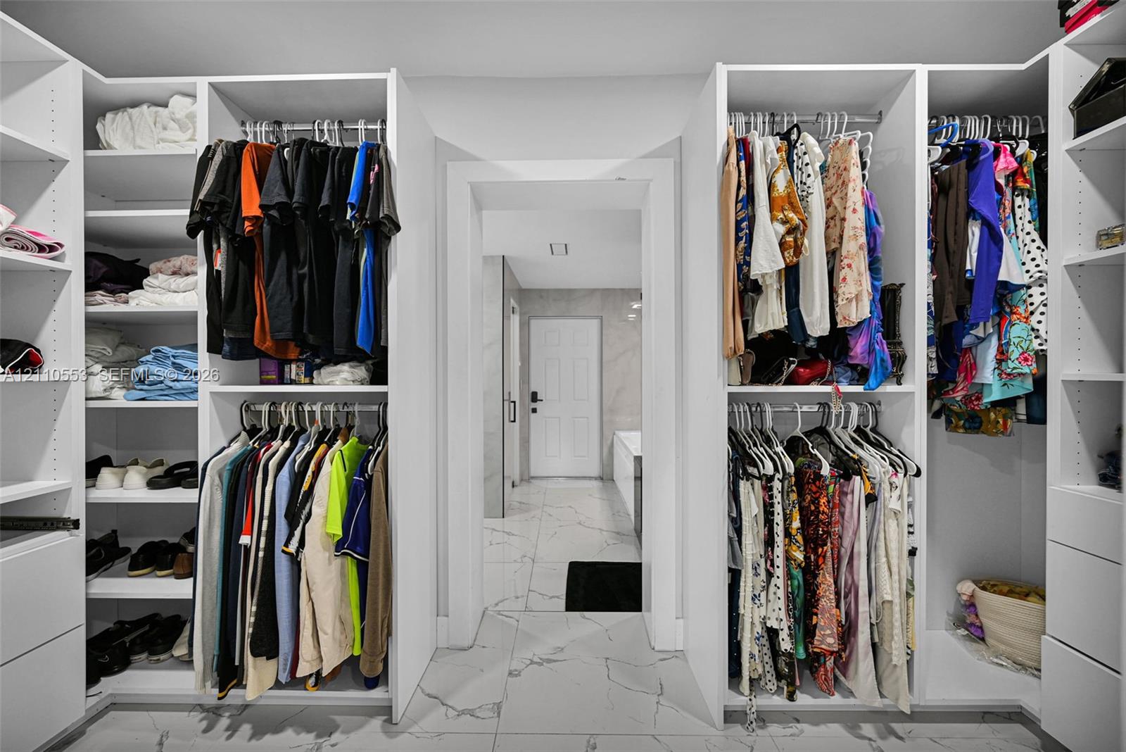 Walk-in dressing area featuring custom white built-in cabinetry, tiered hanging rods, adjustable shelving, and large-format porcelain tile flooring