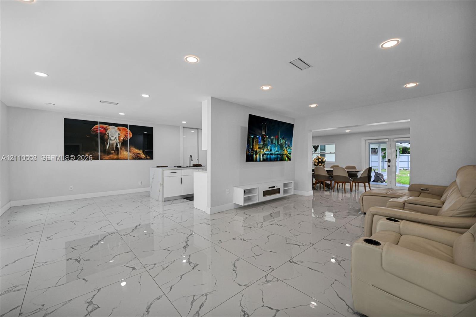 Large-format tile flooring with a neutral-veined pattern, recessed ceiling lighting, kitchen island with cabinetry, and double glass-paneled exterior doors