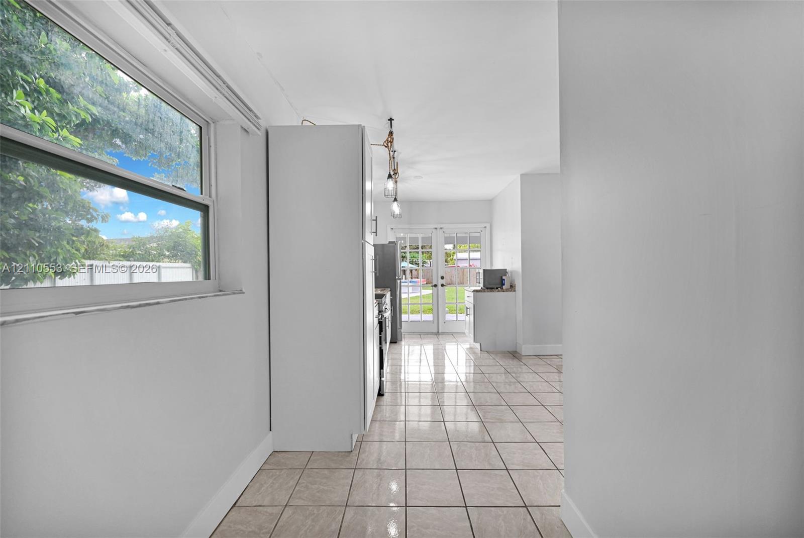 Neutral tile flooring, large single-hung window, white cabinetry, and multi-pane glass french doors