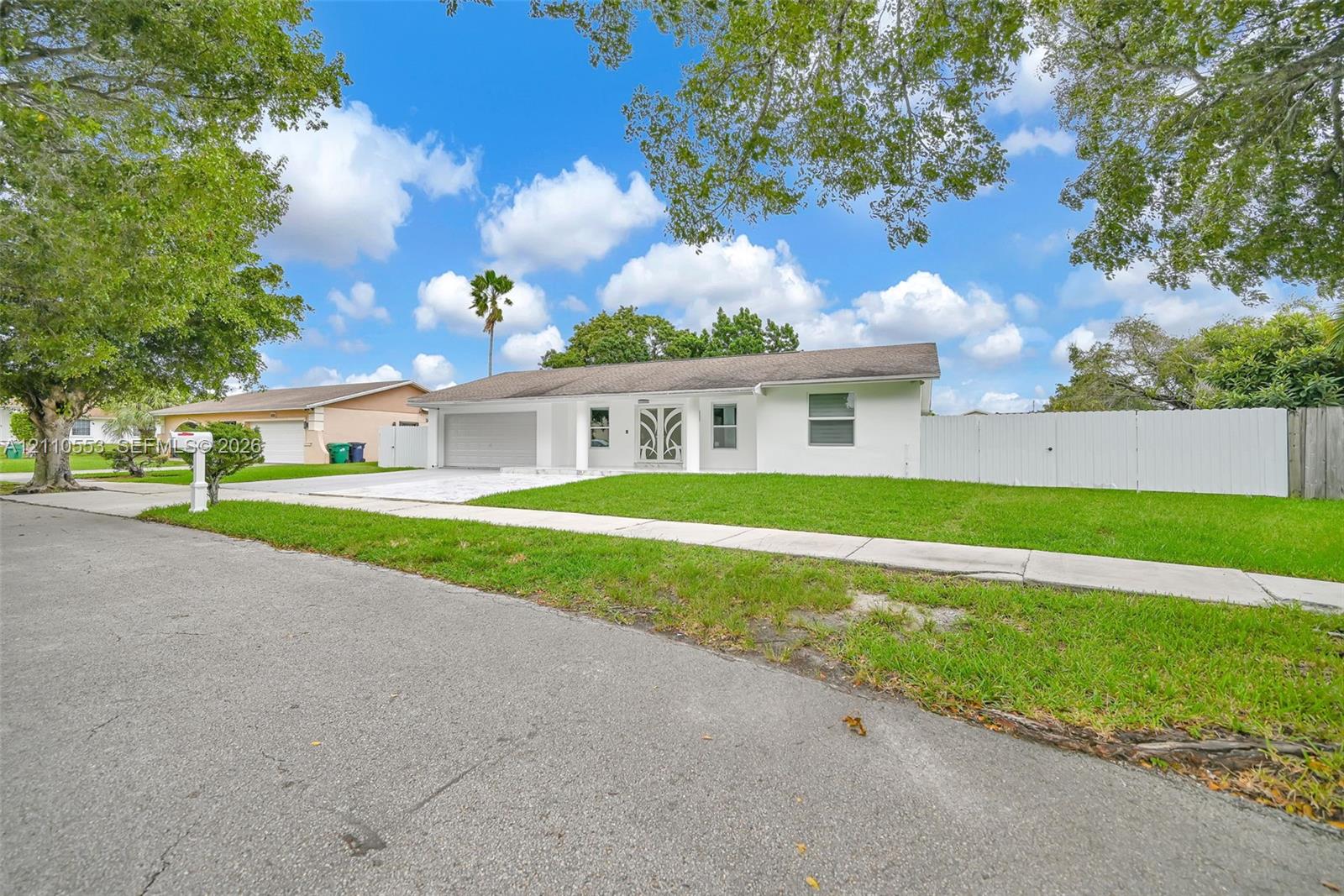 Single-story exterior featuring a painted masonry facade, ornamental glass-paneled entry door, attached two-car garage, and full-perimeter privacy fencing