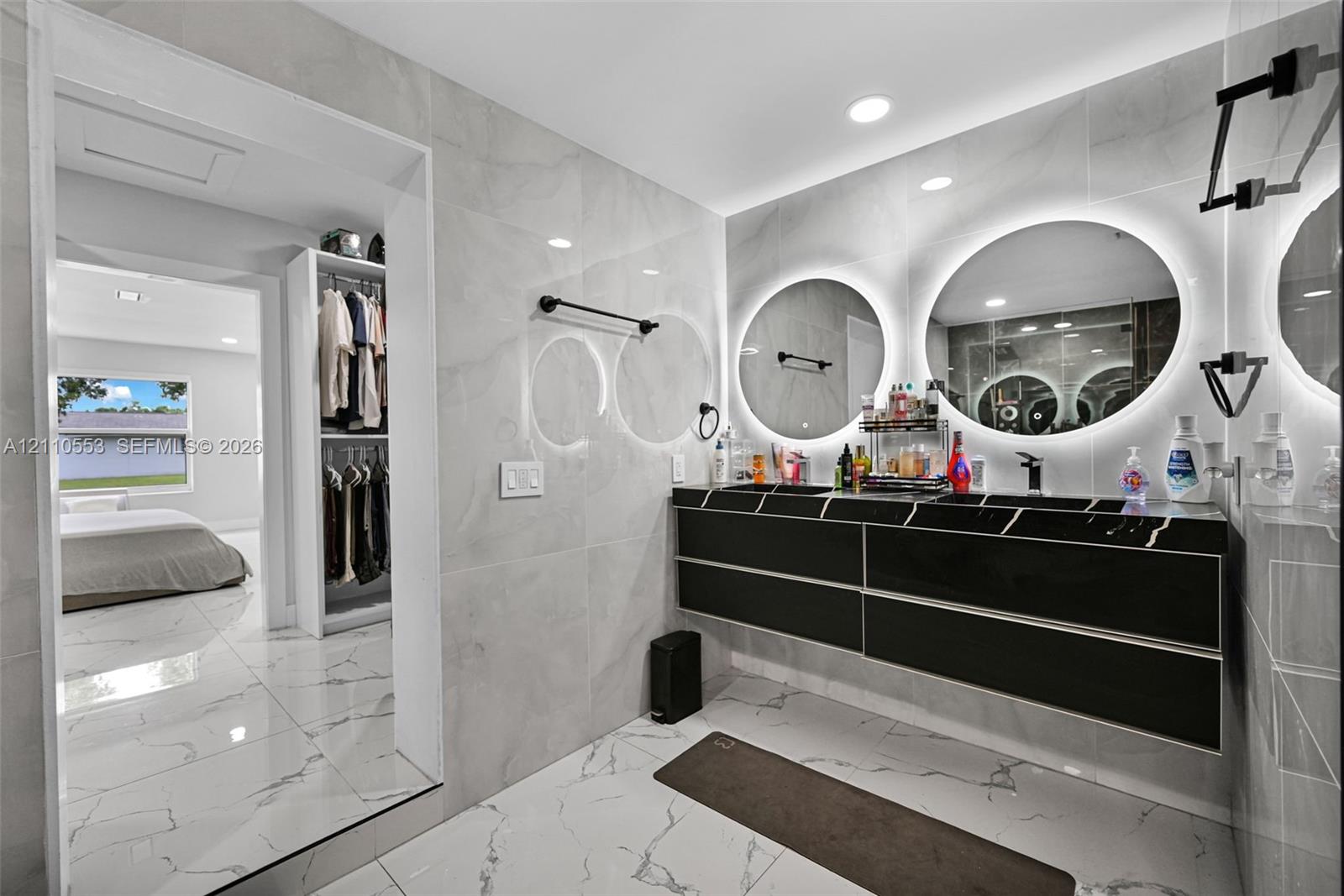 Floating black vanity featuring dual vessel sinks, quartz countertop, large circular backlit mirrors, and floor-to-ceiling large-format wall and floor tile