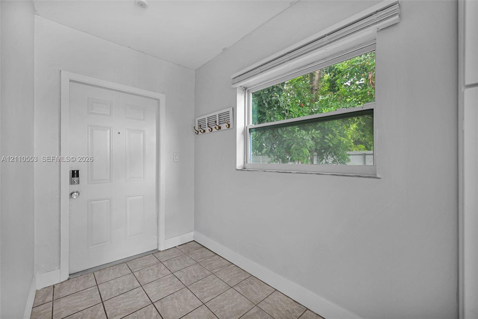 Entry area featuring a solid-core door with electronic deadbolt, ceramic tile flooring, and a single-hung window with horizontal blinds