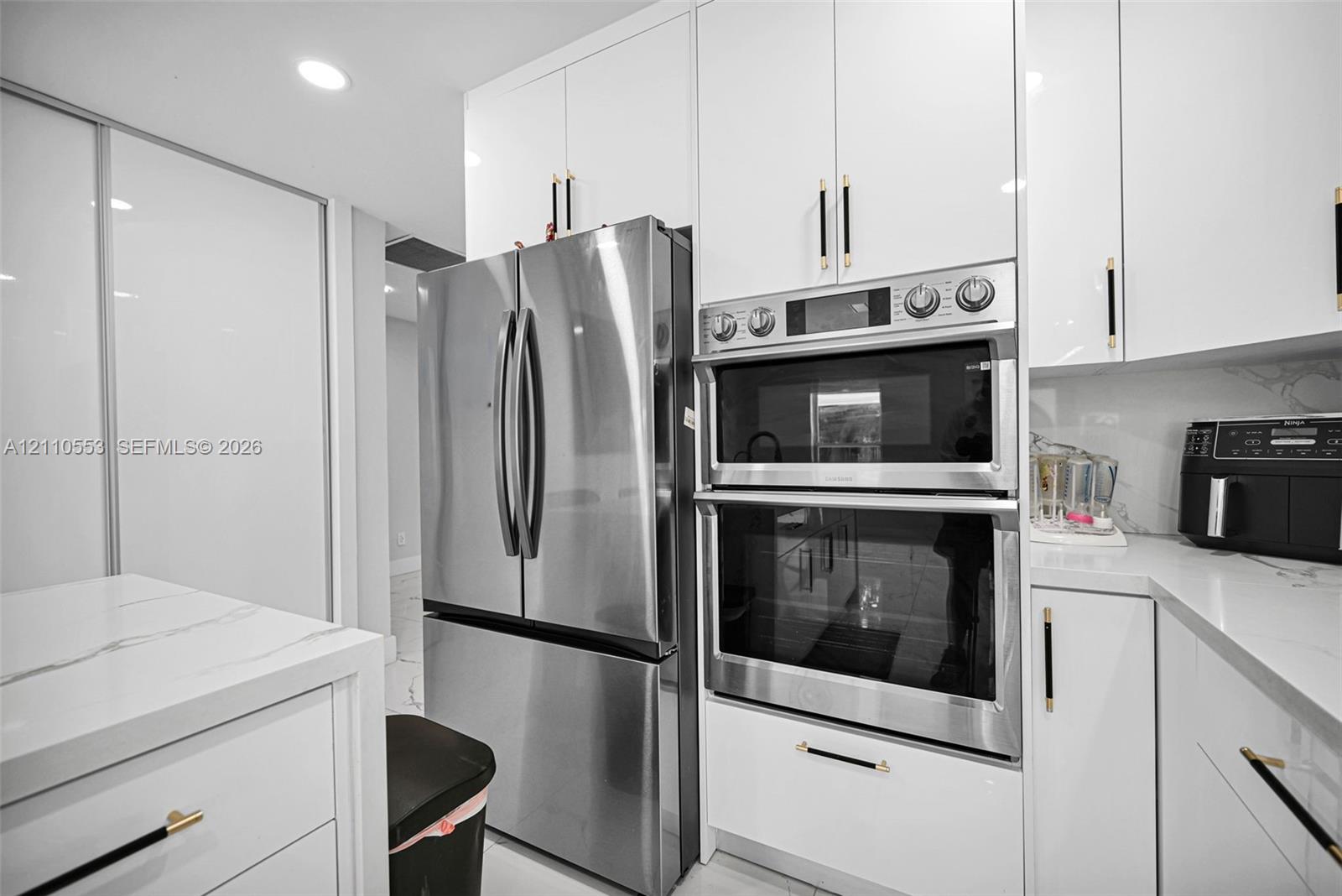 Kitchen featuring high-gloss white cabinetry, stone-finish countertops, stainless steel appliances, a double wall oven, and metallic hardware