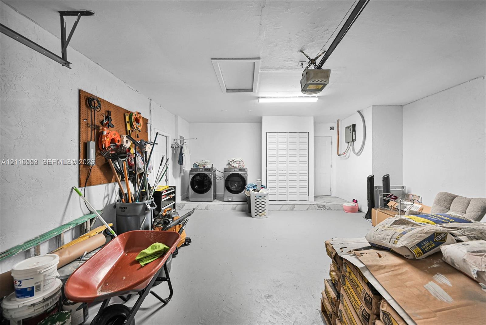 Attached garage featuring a concrete floor, built-in wall storage board, overhead fluorescent lighting, and an integrated laundry area with louvered closet doors
