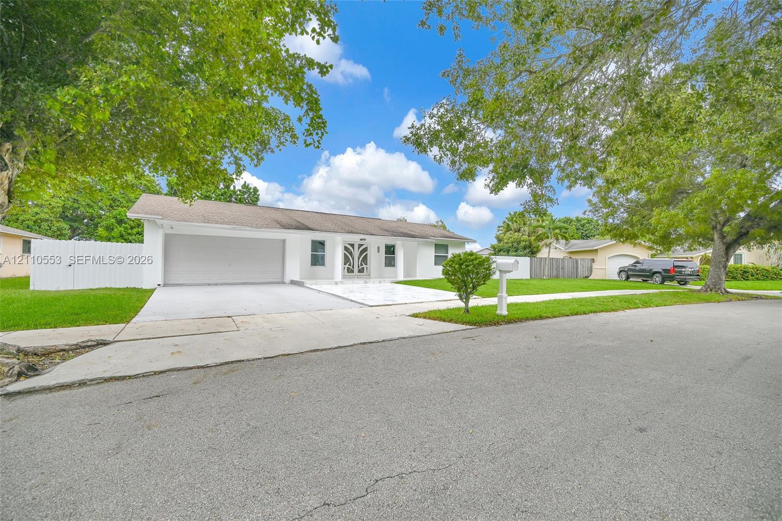 Single-story exterior featuring white stucco siding, a two-car garage, a decorative metal-frame front door, a concrete driveway, and white vinyl privacy fencing