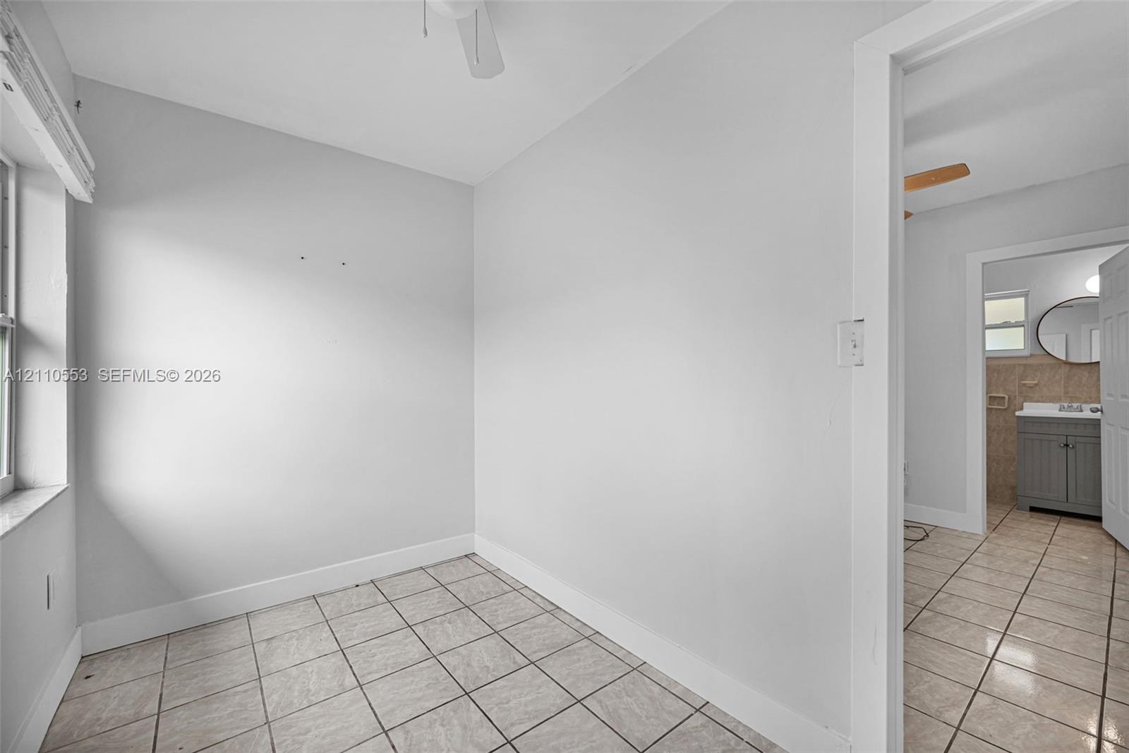 Neutral-toned interior space featuring light-colored ceramic tile flooring, a ceiling-mounted fan, and natural light via a single window