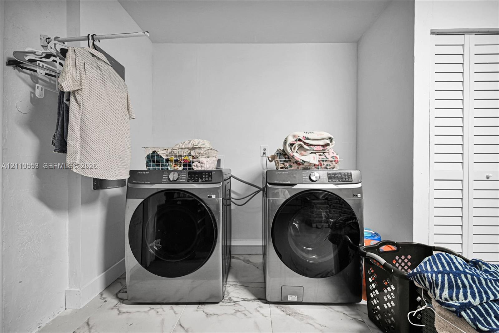 Laundry space featuring stone-pattern flooring, wall-mounted hanging rod, and louvered closet doors