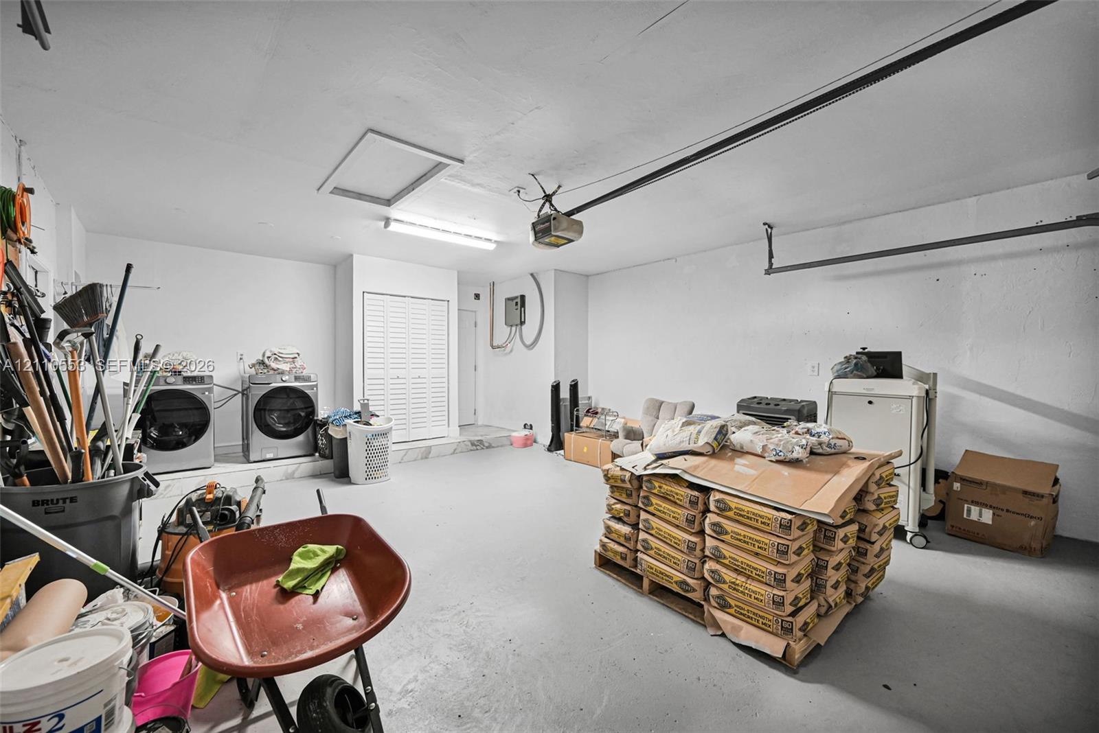Garage space featuring a painted concrete floor, ceiling-mounted garage door opener, overhead lighting, and dedicated laundry hookups with bifold closet doors