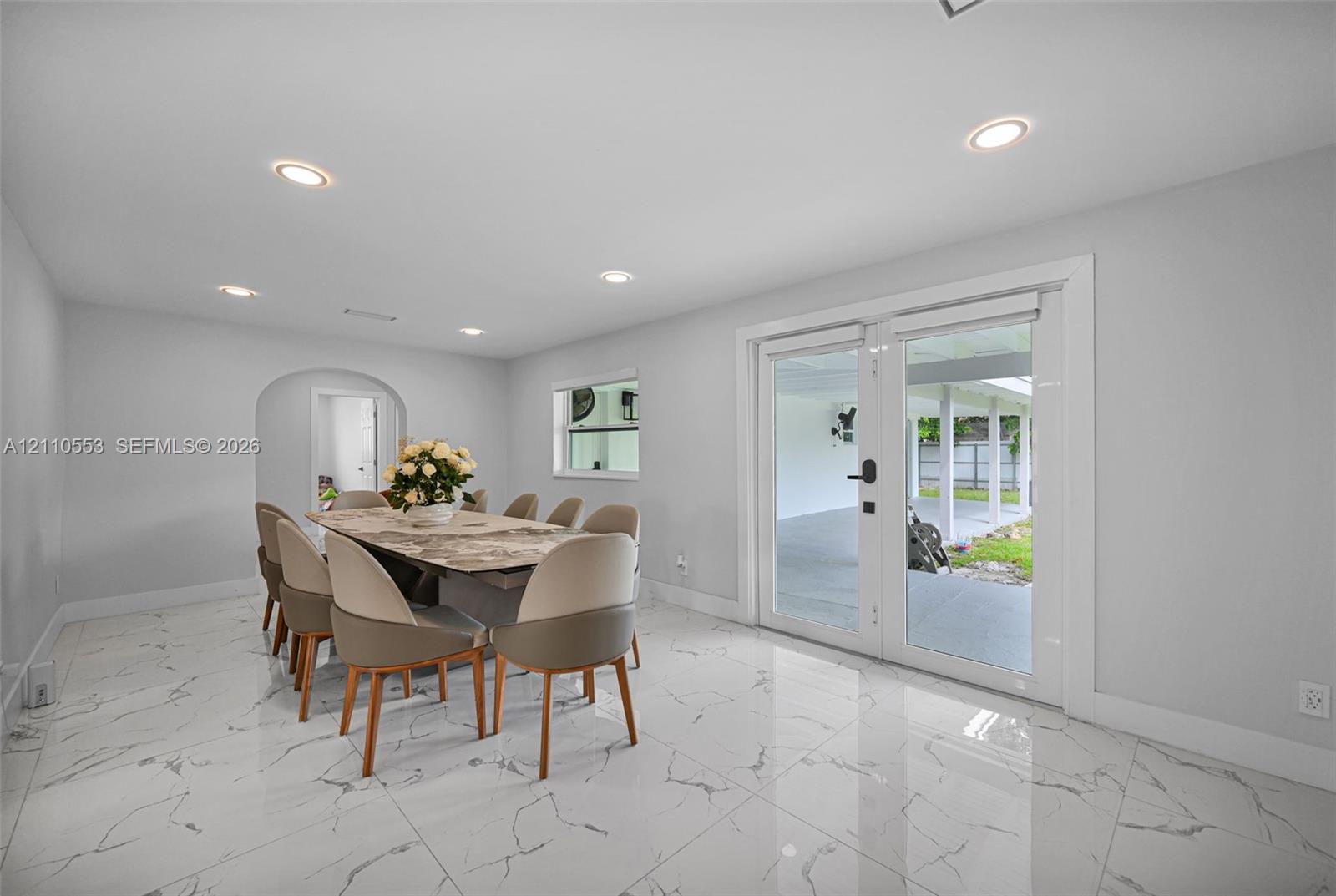Large-format stone-patterned tile flooring, recessed ceiling lighting, arched entryway, and glass-paneled double doors providing exterior access