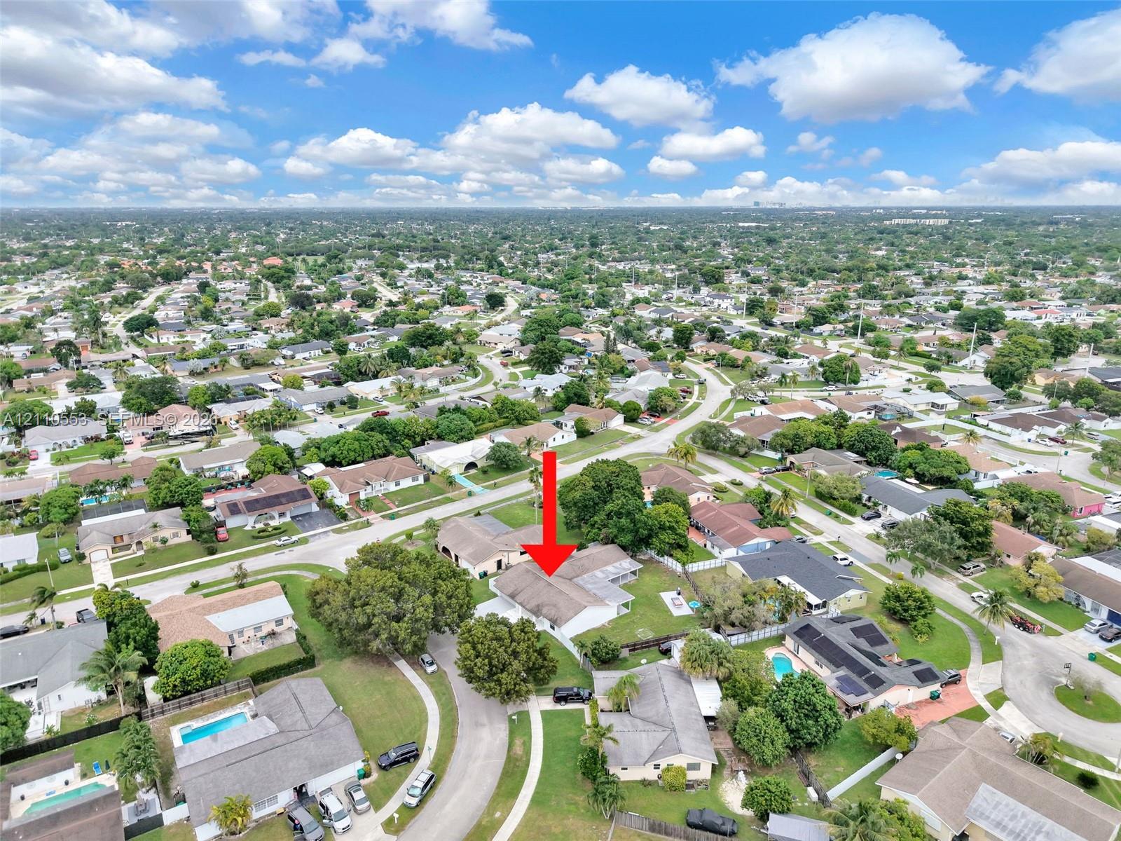Aerial perspective featuring a single-story residence with a multi-gabled roofline and an attached garage, situated on a corner lot with mature landscaping
