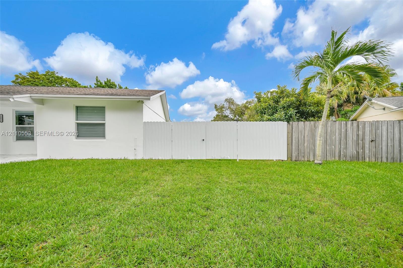 Backyard featuring a manicured lawn, white vinyl privacy fencing, natural wood-finish fencing, and mature palm tree