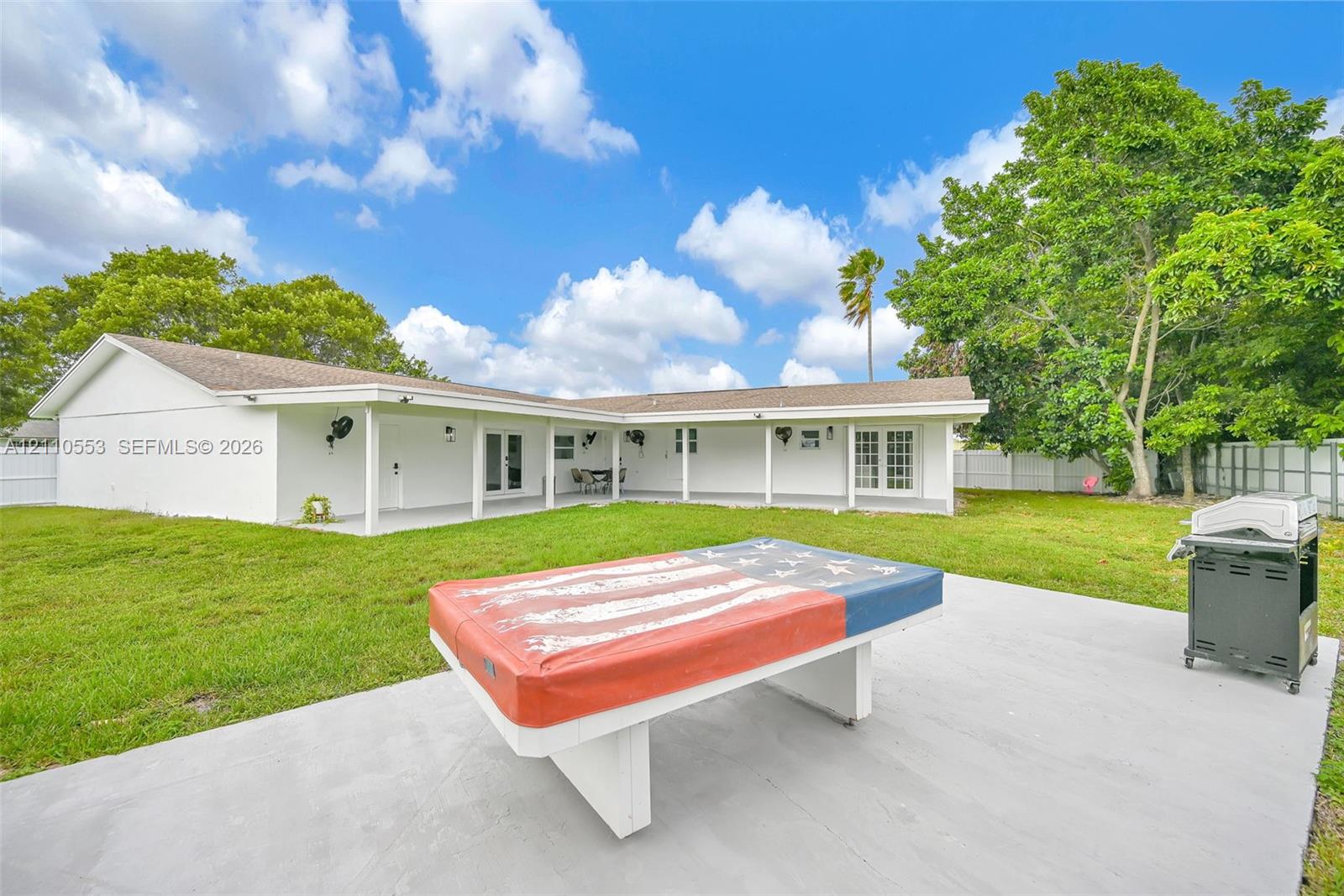 Expansive backyard featuring a manicured lawn, concrete patio, covered porch, and perimeter privacy fencing