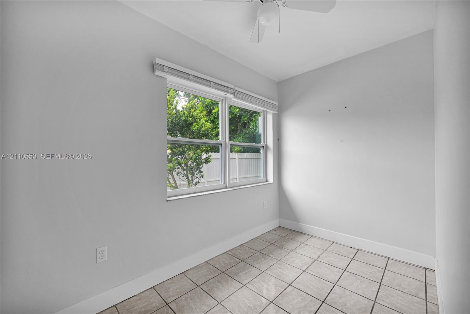 Neutral-toned room featuring tile flooring, a dual-pane window with white blinds, and a ceiling-mounted light fixture with a fan