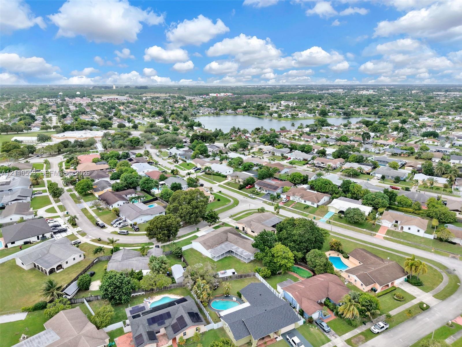 Aerial perspective of a residential neighborhood featuring established tree canopy, diverse housing styles, and a central lake