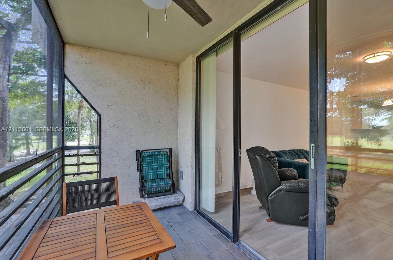 Screened-in balcony featuring grey wood-finish flooring, a ceiling fan, and large sliding glass doors