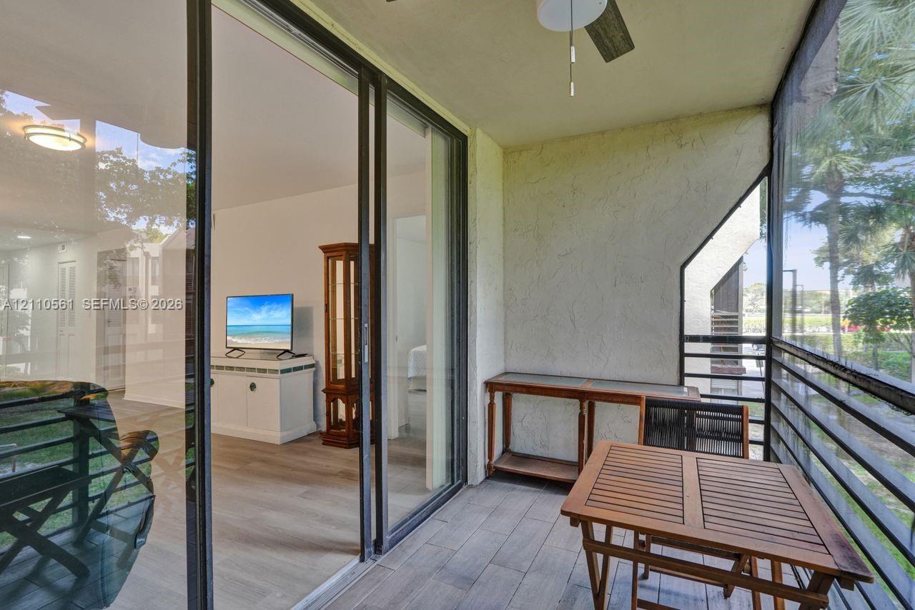 Screened balcony featuring wood-finish flooring, a ceiling fan, and sliding glass door access