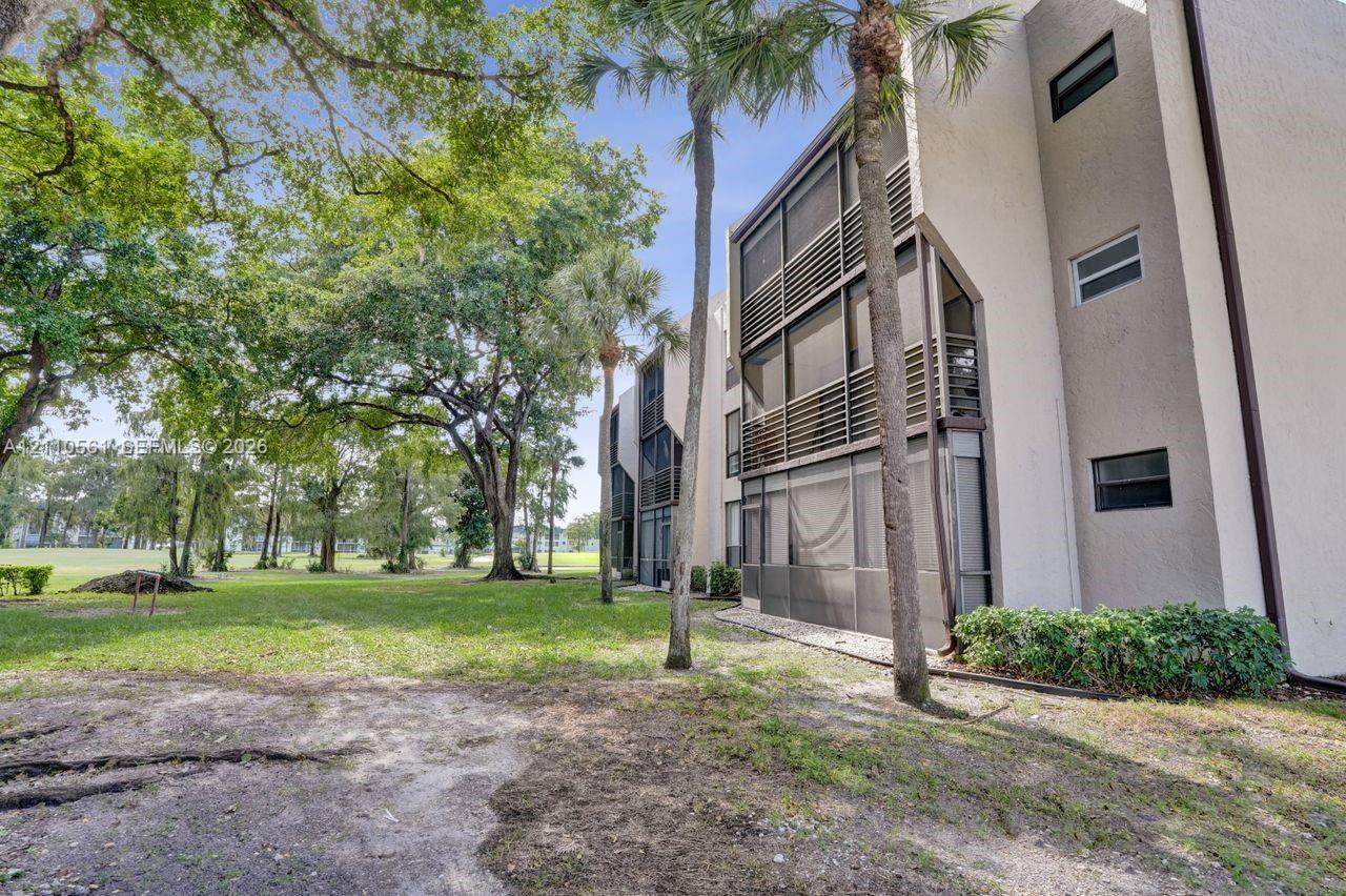 Multi-story residential building exterior featuring stucco siding, multi-level screened-in balconies, and mature landscaping