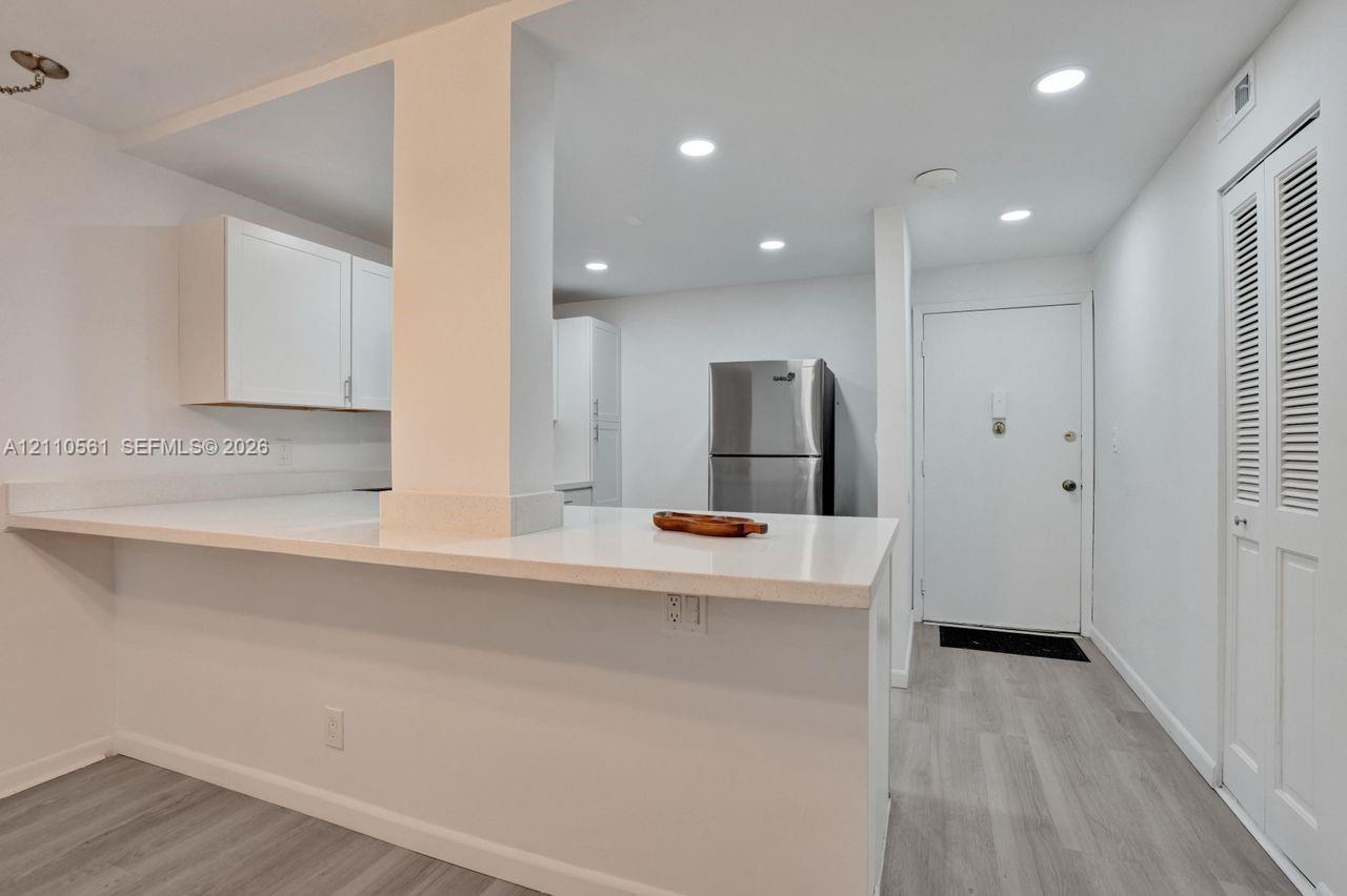 Kitchen featuring a white peninsula with a solid-surface countertop, flat-panel white cabinetry, recessed lighting, wood-finish flooring, and stainless steel refrigerator