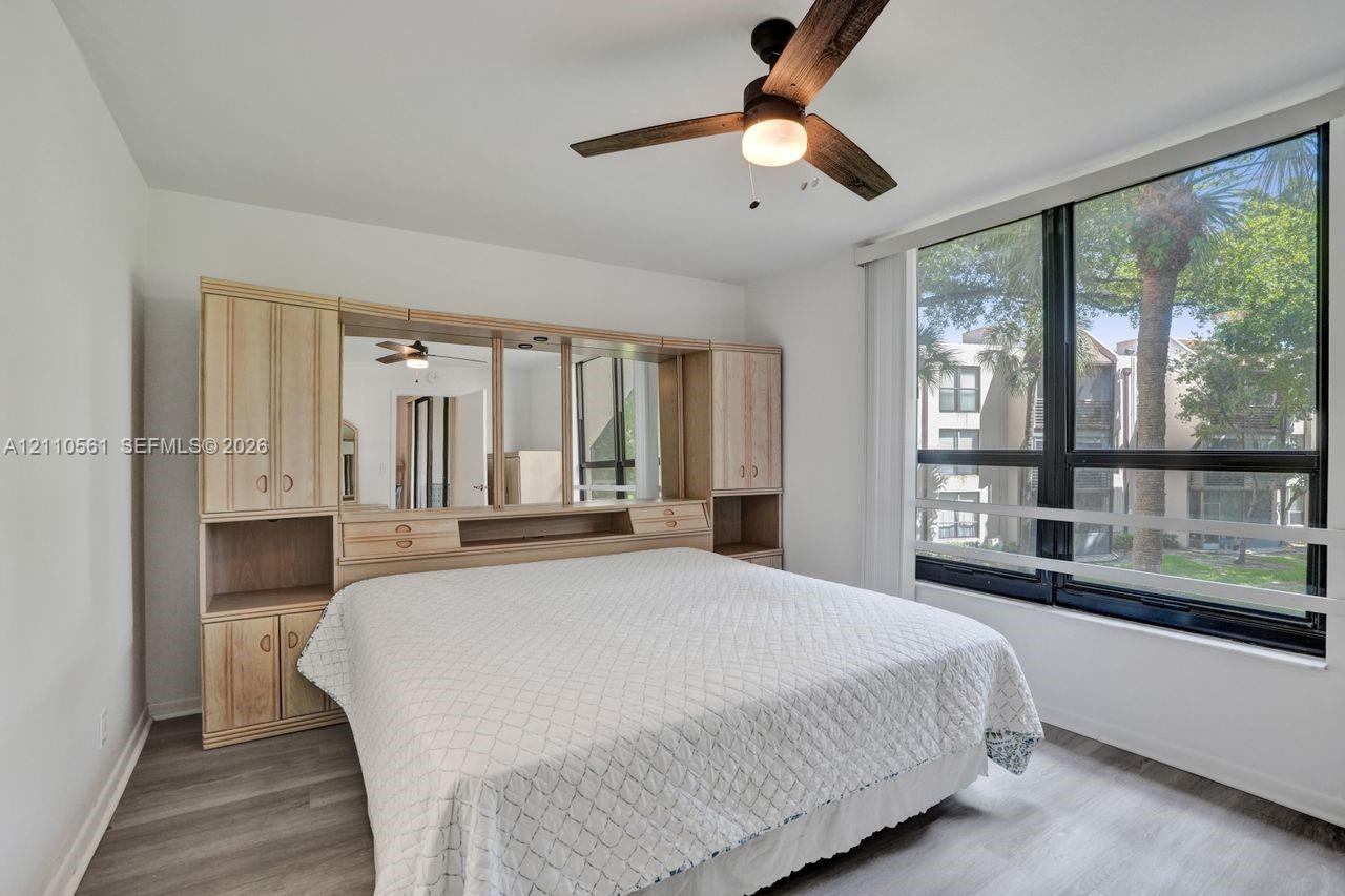 Room featuring wood-finish flooring, built-in light-colored cabinetry with integrated shelving and mirrored accents, and floor-to-ceiling windows with horizontal mullions, complemented by a ceiling fan with light fixture