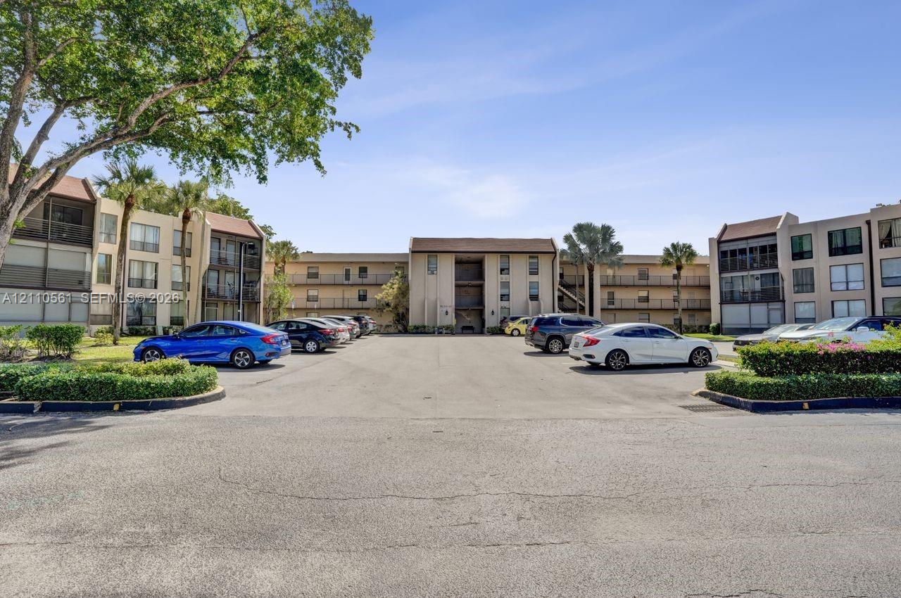 Multi-story exterior featuring a neutral stucco facade, shingled roofing, integrated balconies, and mature landscaping