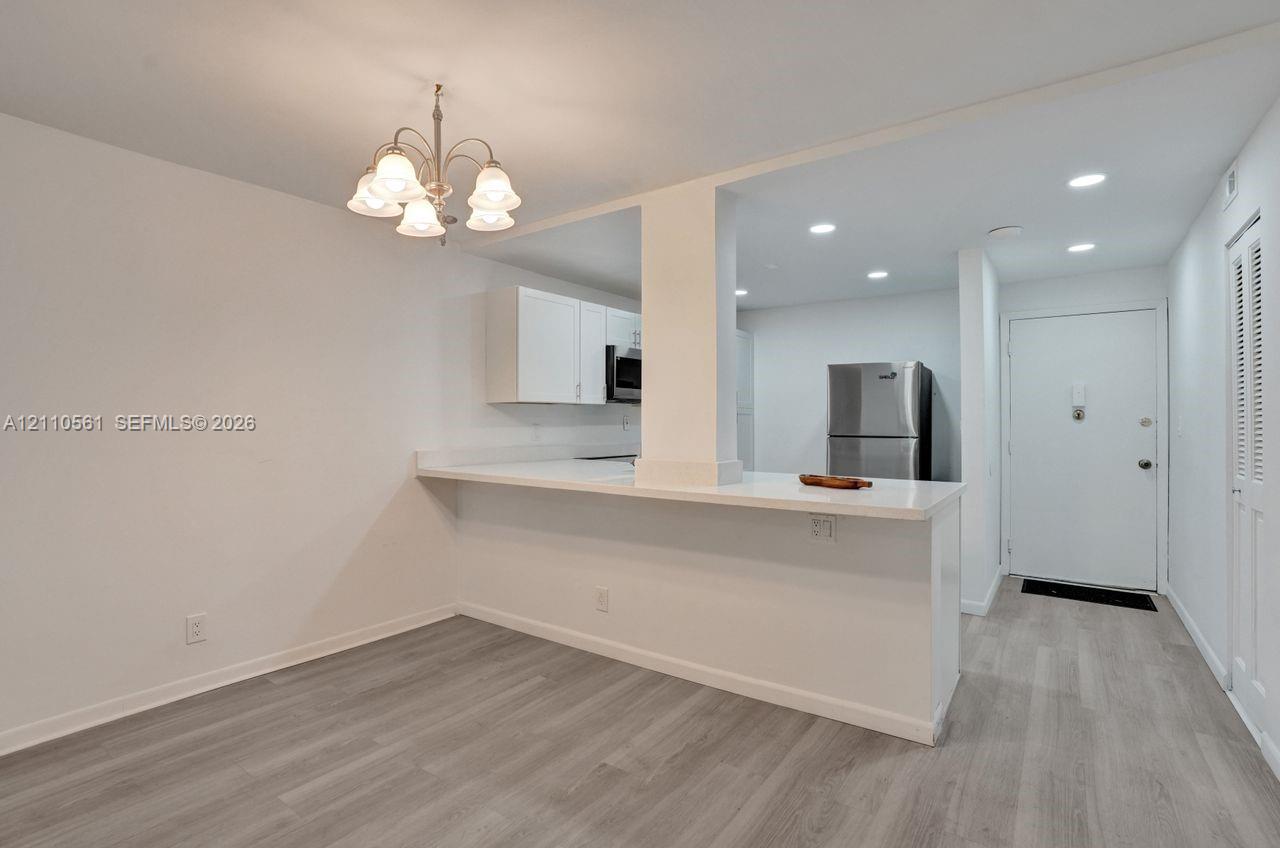 Kitchen featuring a peninsula with solid-surface countertop, white cabinetry, stainless steel refrigerator, recessed lighting, and wood-finish flooring