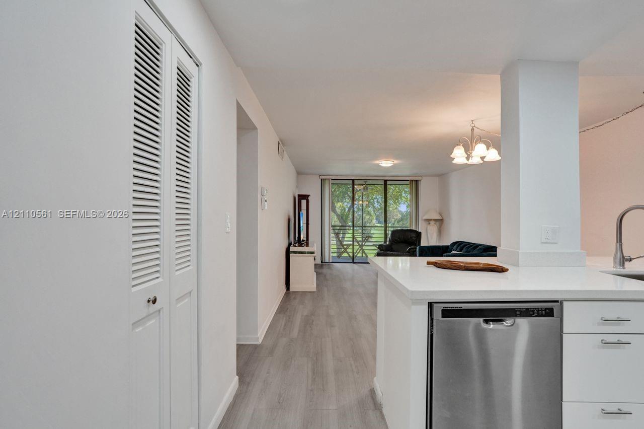 Interior space featuring wood-finish flooring, white cabinetry, integrated stainless steel dishwasher, louvered-door closet, and sliding glass balcony doors