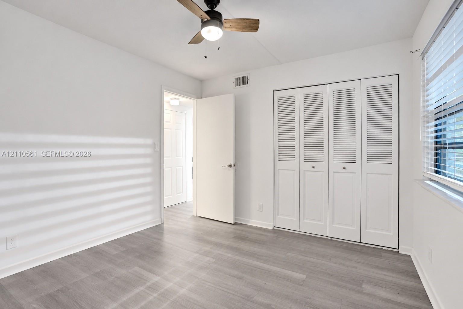 Wood-finish flooring, white louvered closet doors, and a ceiling fan with integrated lighting