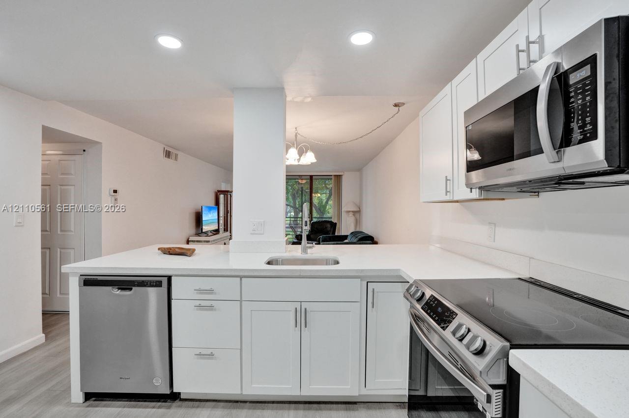 Kitchen featuring white cabinetry, solid-surface countertops, recessed lighting, and stainless steel appliances, including an over-the-range microwave, dishwasher, and electric range