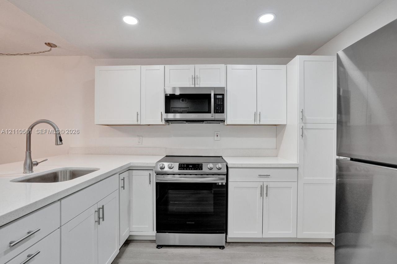 Kitchen featuring white shaker-style cabinetry, quartz countertops, stainless steel appliances, a pull-down kitchen faucet, and recessed lighting