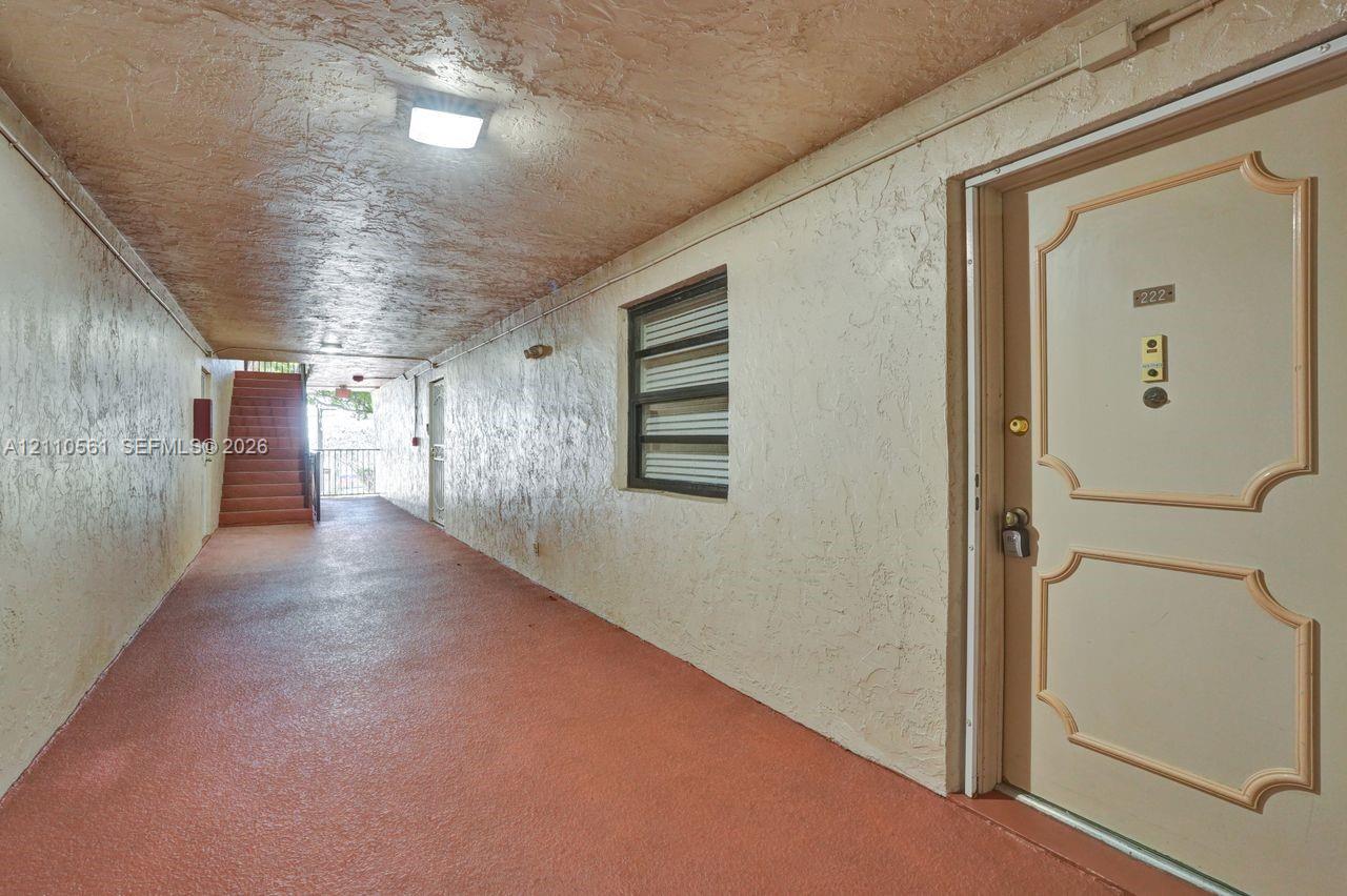 Covered exterior walkway with textured ceiling, flush-mount lighting, and solid-core paneled entry door