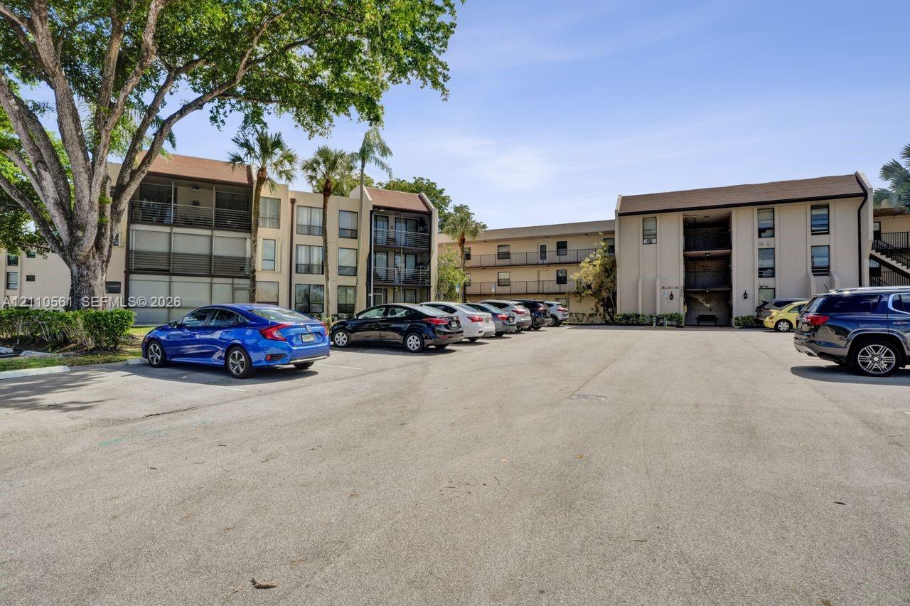 Multi-story complex exterior featuring neutral stucco siding, pitched roofs, screen-enclosed balconies, and mature landscaping
