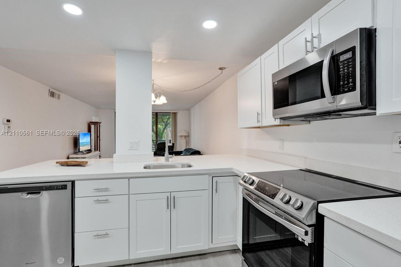 Kitchen featuring white cabinetry, solid-surface countertops, recessed ceiling lighting, and stainless steel appliances including a microwave, dishwasher, and range