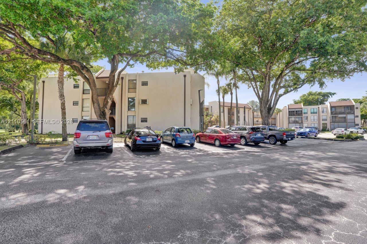 Multi-story stucco exterior buildings featuring paved surface parking and mature canopy trees
