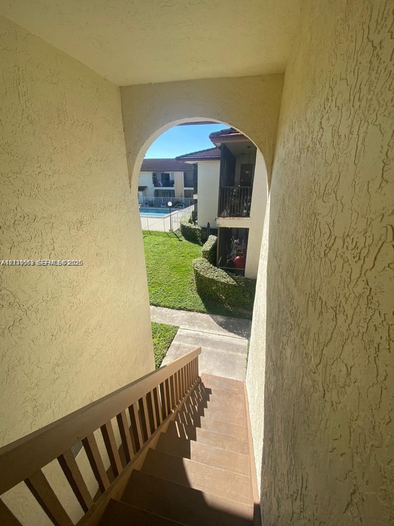 Exterior staircase featuring stucco walls, an arched entryway, and wooden handrail, with grounds displaying manicured landscaping and a swimming pool Exterior staircase featuring stucco walls, an arched entryway, and wooden handrail, with grounds displaying manicured landscaping and a swimming pool