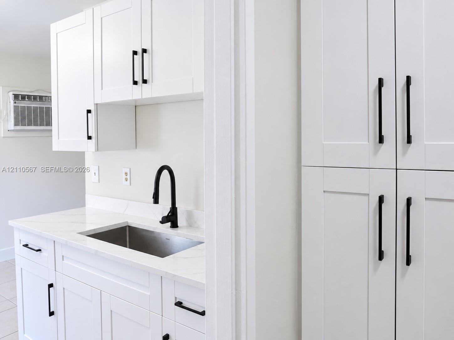 White shaker-style cabinetry with matte black hardware, stone-finish countertops, stainless steel undermount sink, and high-arch matte black faucet