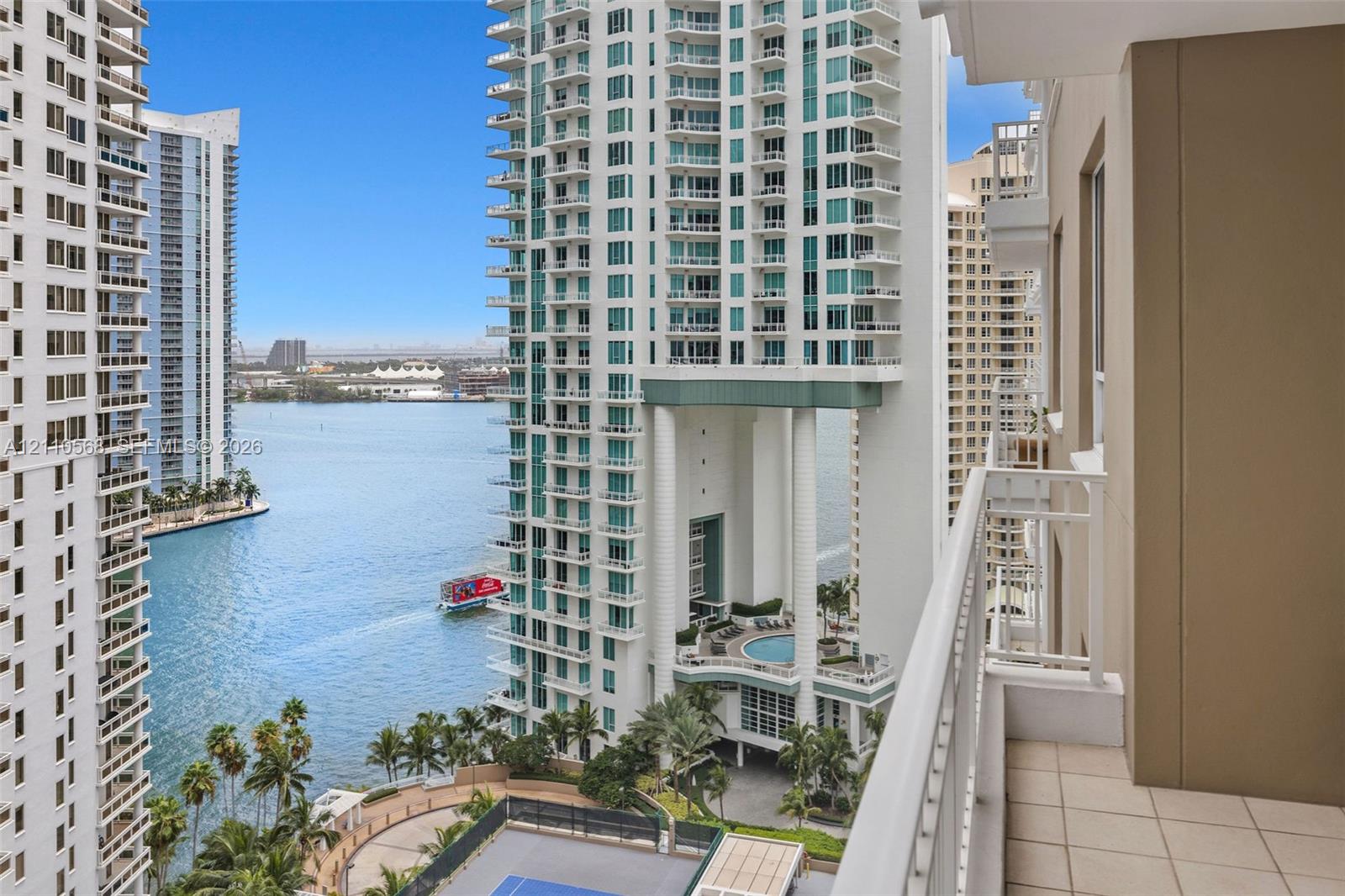 Covered balcony featuring tile flooring and a white metal railing, overlooking the water and metropolitan skyline